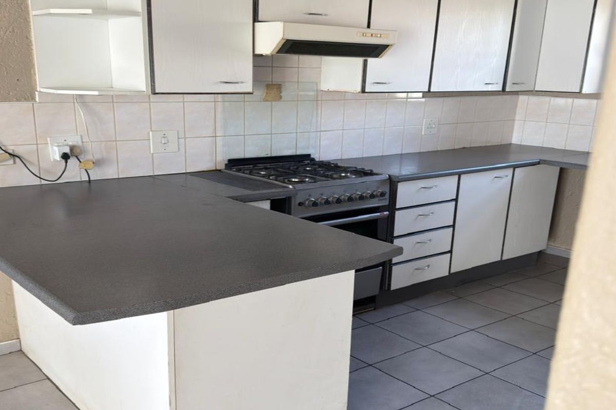 A functional kitchen featuring white cabinetry, dark laminate countertops, a gas stove with extractor fan, and tiled flooring, offering a clean, blank canvas for updates.