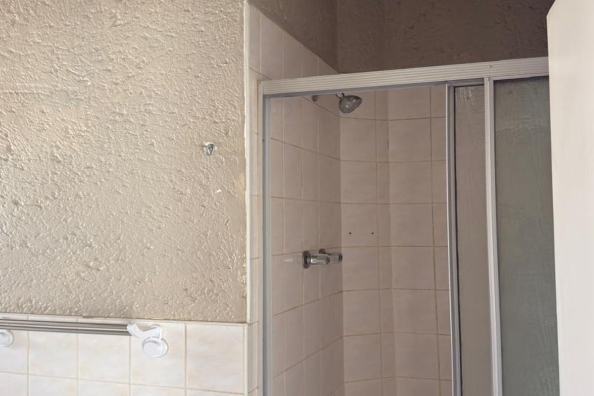 A dated bathroom featuring a tiled shower enclosure with a sliding door and a wall-mounted towel rail.