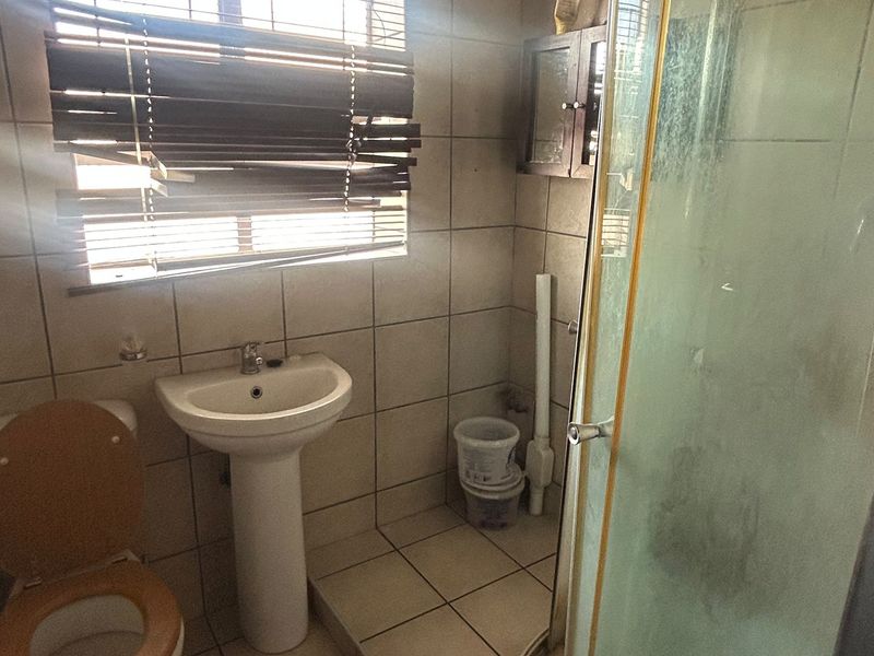 A functional bathroom featuring a pedestal basin, toilet, and shower enclosure with tiled finishes throughout.