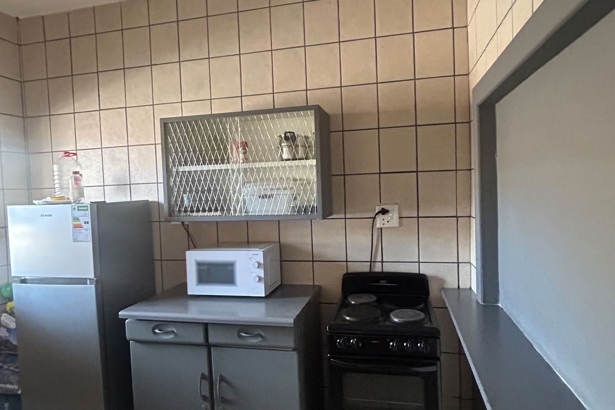 A functional kitchen area featuring tiled wall splashbacks, built-in base cabinetry, and an electric stove, offering a practical layout for daily cooking needs.
