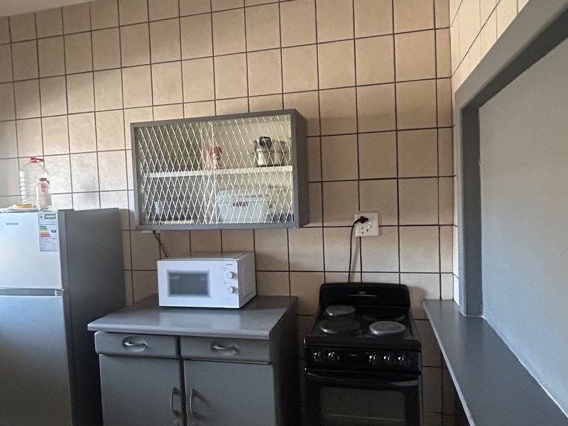 A functional kitchen area featuring tiled wall splashbacks, built-in base cabinetry, and an electric stove, offering a practical layout for daily cooking needs.