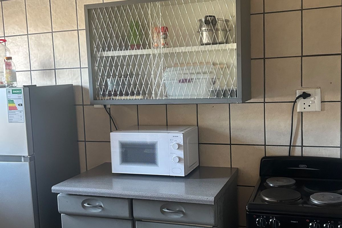 A functional kitchen area featuring tiled walls, a wall-mounted cabinet, countertop space with built-in drawers, and a freestanding electric stove.
