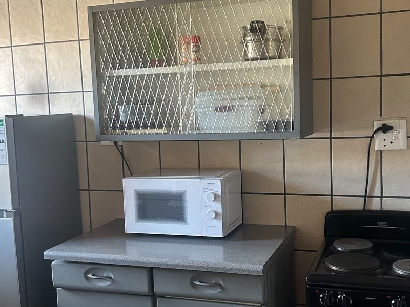 A functional kitchen area featuring tiled walls, a wall-mounted cabinet, countertop space with built-in drawers, and a freestanding electric stove.