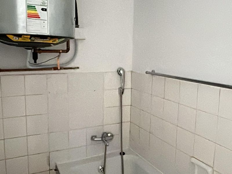 A functional bathroom featuring a wall-mounted electric water heater, tiled walls, and a shower mixer with a handheld shower head.