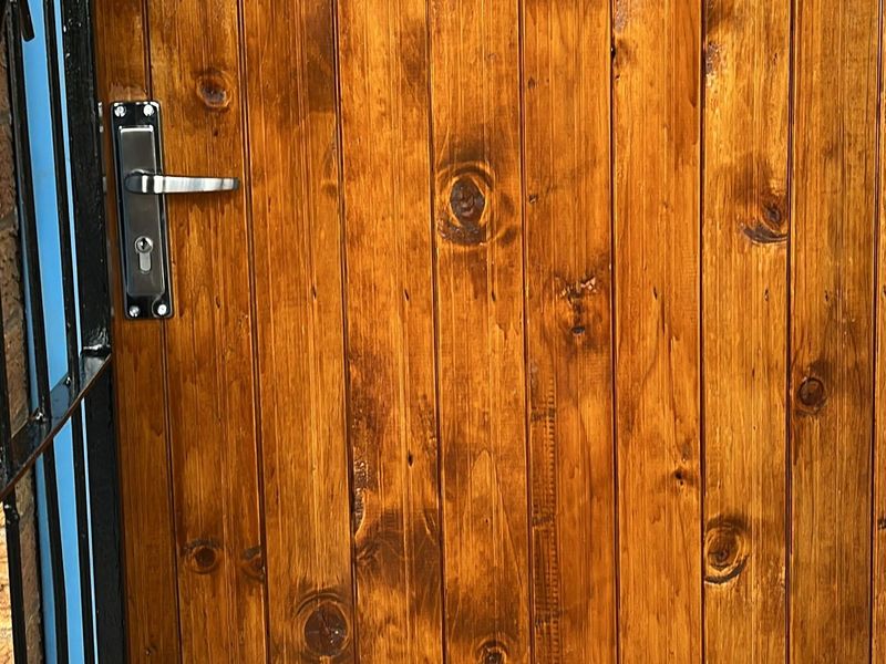 A close-up view of a timber entrance door featuring a metal security gate and standard lever handle lockset.