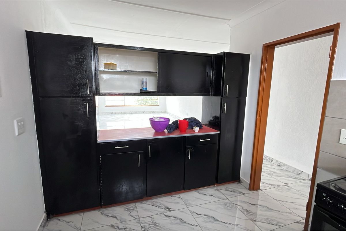 A kitchen area featuring black built-in cabinetry, tiled flooring, and a functional electric stove, offering potential for modern updates.