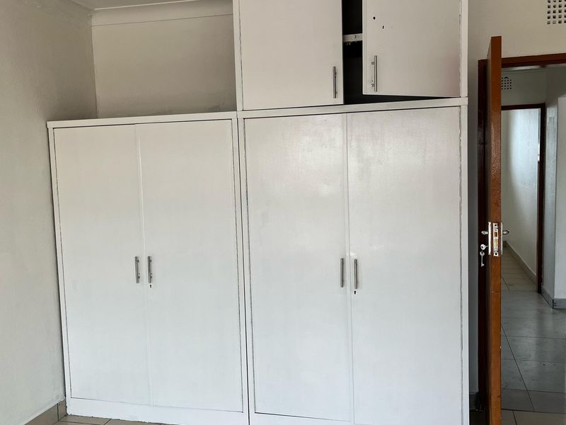 A bedroom featuring built-in white cupboards with some visible wear and maintenance requirements, leading into a tiled hallway.