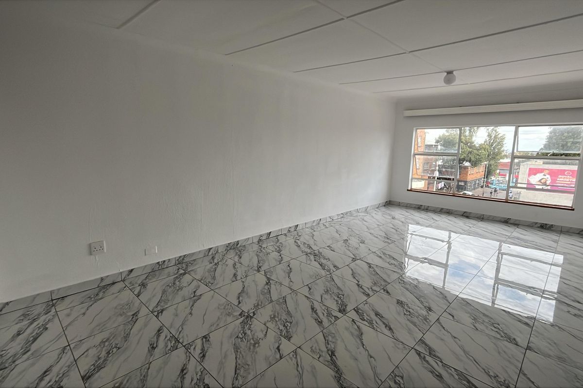 A bright, empty living area featuring modern marble-look floor tiles, a large window with urban views, and a clean, neutral aesthetic.