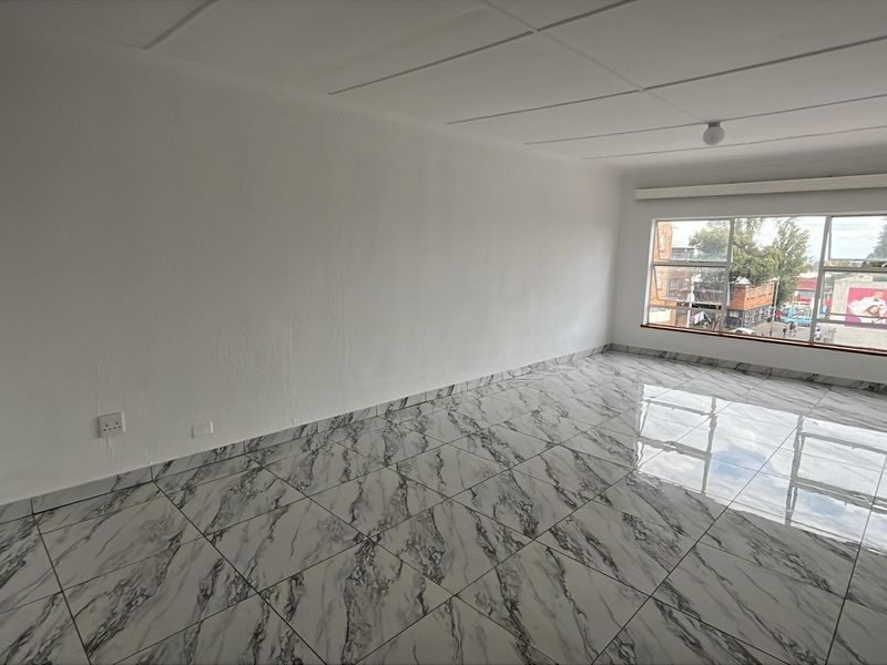 A bright, empty living area featuring modern marble-look floor tiles, a large window with urban views, and a clean, neutral aesthetic.
