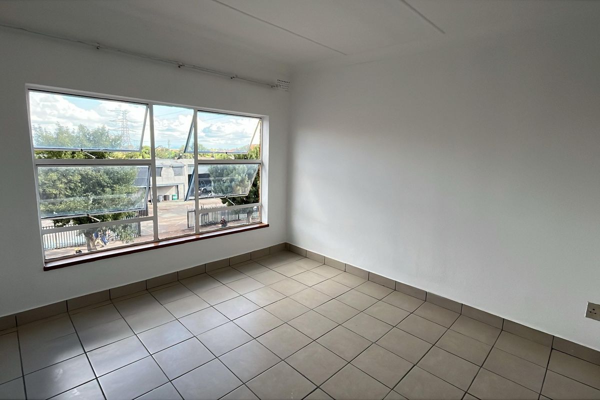A bright, empty bedroom featuring neutral tiled flooring and a large window providing natural light and street views.
