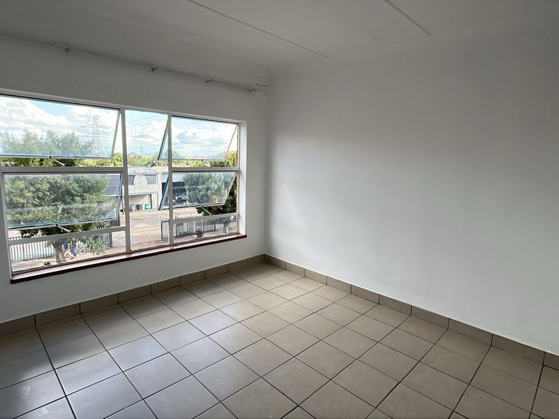 A bright, empty bedroom featuring neutral tiled flooring and a large window providing natural light and street views.