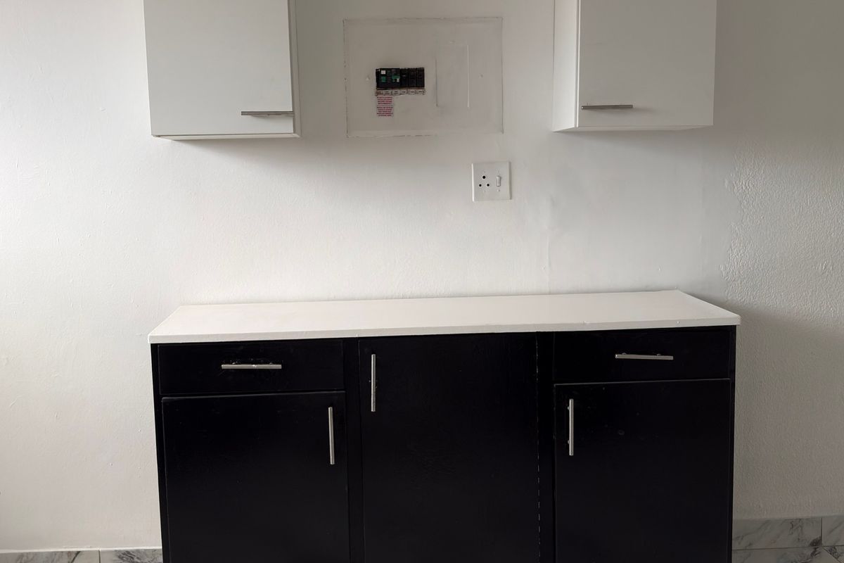 A clean kitchen area featuring black base cabinets, white wall-mounted storage, and a white countertop, providing a functional and modern workspace.