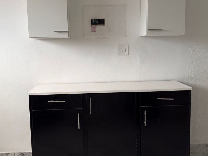 A clean kitchen area featuring black base cabinets, white wall-mounted storage, and a white countertop, providing a functional and modern workspace.
