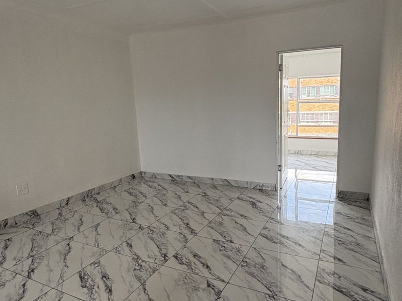 A bright, empty bedroom featuring modern marble-effect floor tiles and a doorway leading to an adjacent balcony area.
