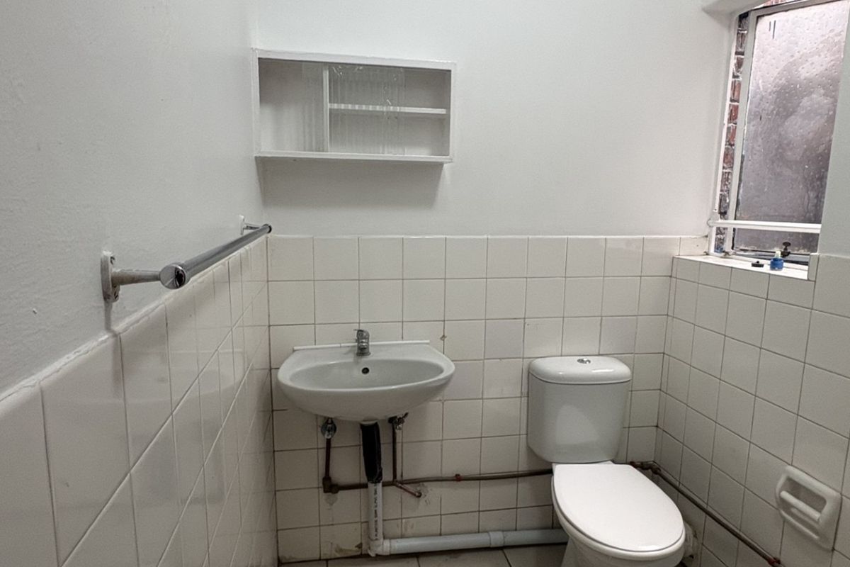 A functional bathroom featuring a wall-mounted basin, toilet, and tiled walls. The space is ready for modernization and cosmetic updates.