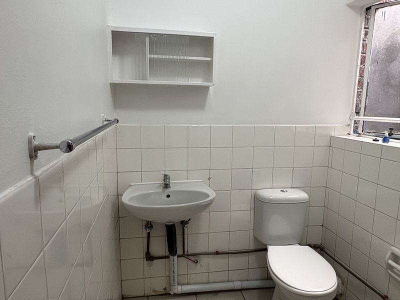 A functional bathroom featuring a wall-mounted basin, toilet, and tiled walls. The space is ready for modernization and cosmetic updates.
