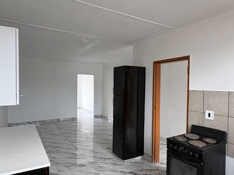A functional kitchen area featuring tiled flooring, a tiled backsplash, and built-in cabinetry, leading into an open-plan living space.