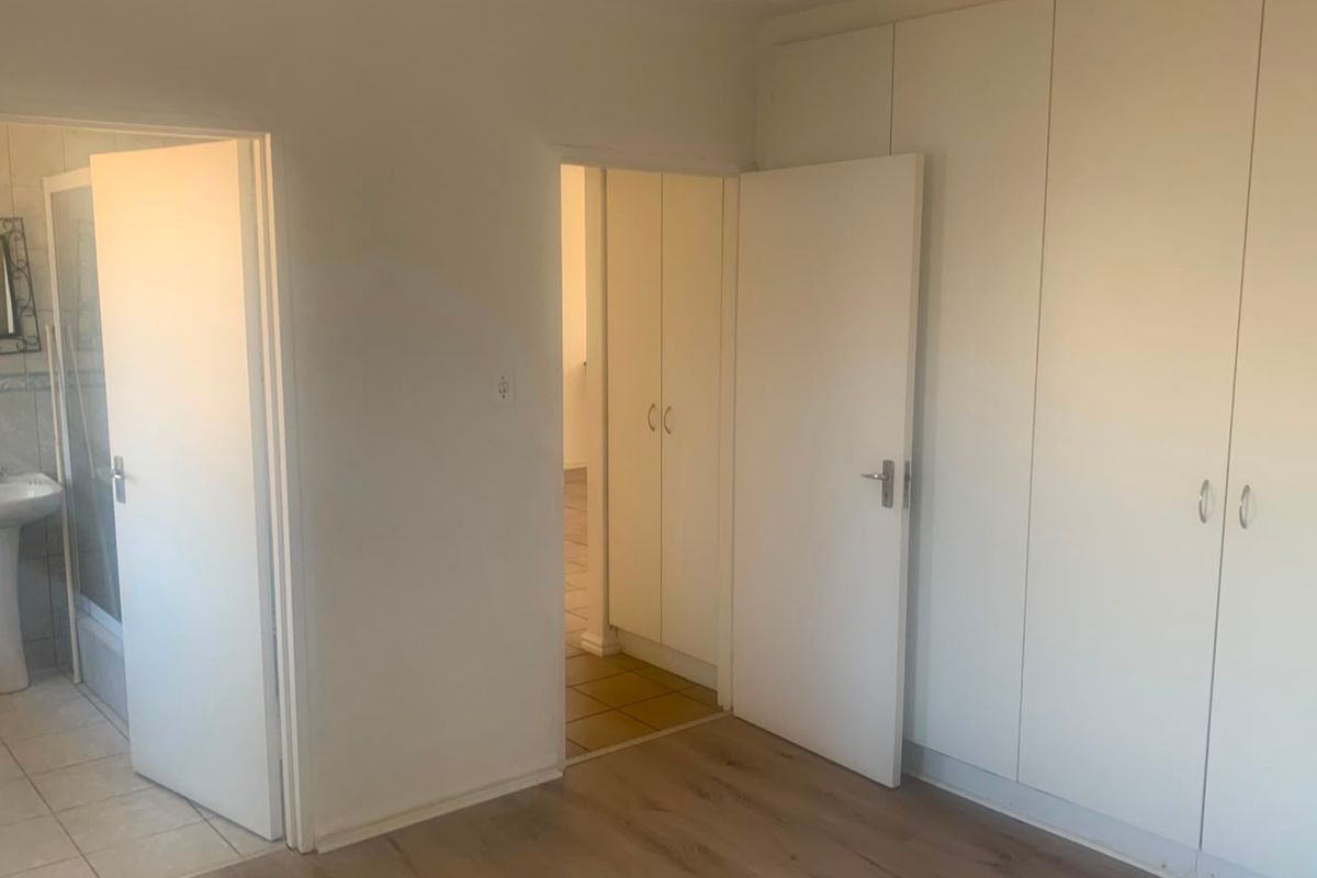An empty bedroom featuring built-in cupboards, laminate flooring, and an adjoining en-suite bathroom with a pedestal basin.