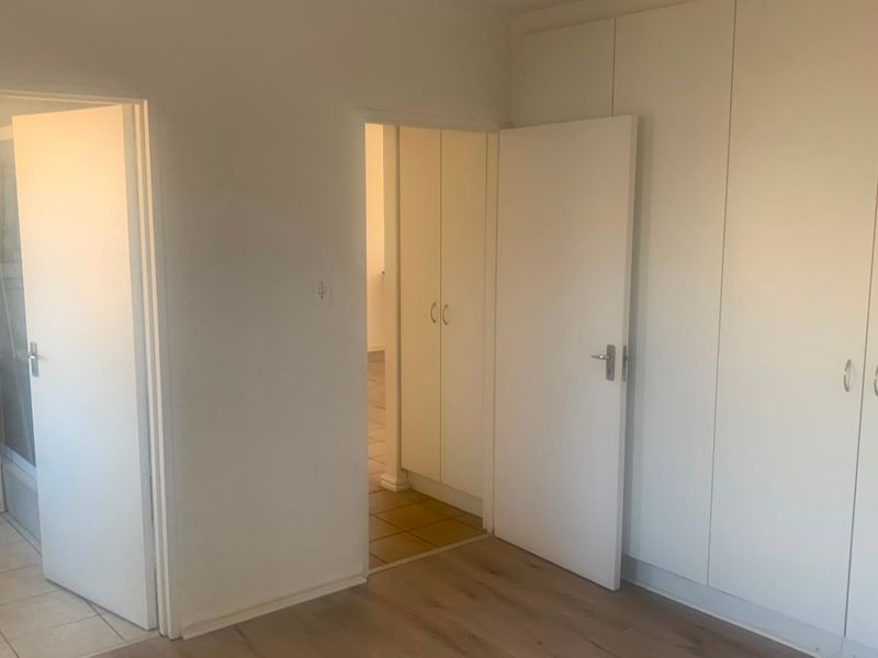 An empty bedroom featuring built-in cupboards, laminate flooring, and an adjoining en-suite bathroom with a pedestal basin.