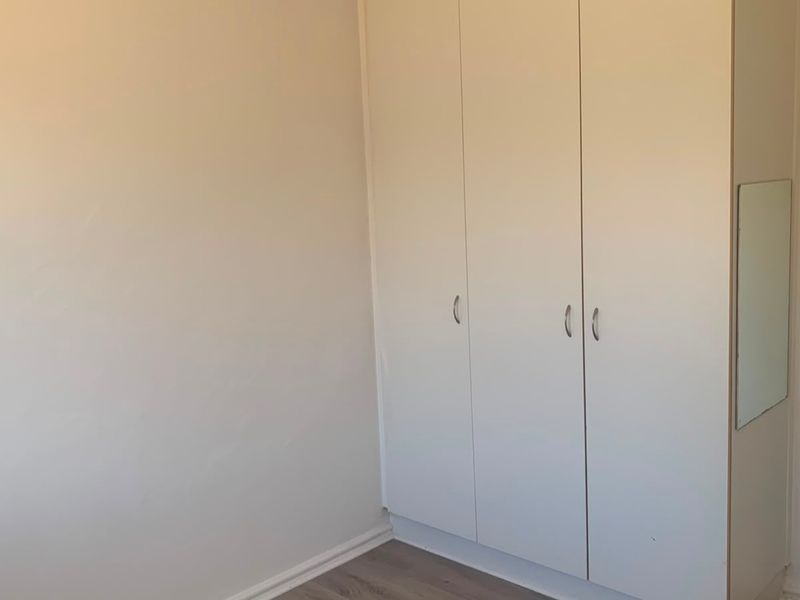A clean, empty bedroom featuring neutral walls, laminate flooring, and a functional built-in wardrobe with white cabinetry.