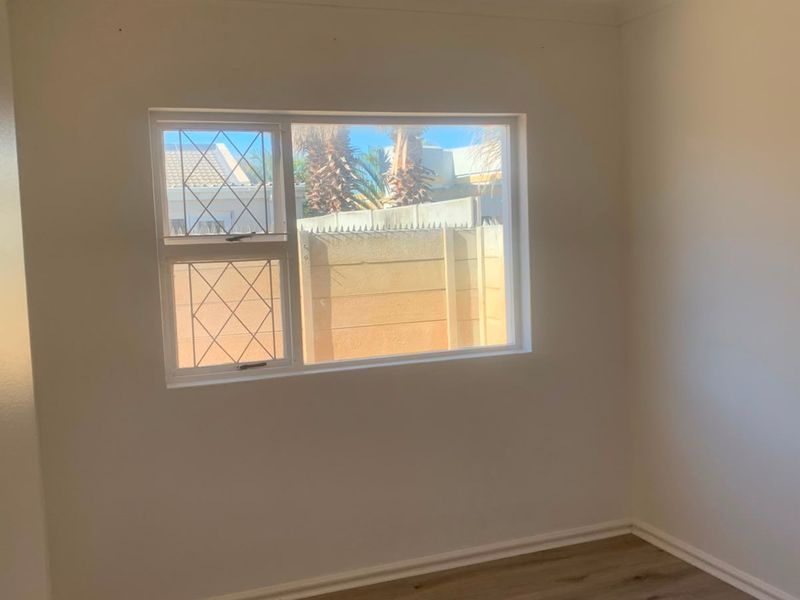 A bright, empty bedroom featuring neutral walls, modern laminate flooring, and a window fitted with security bars.