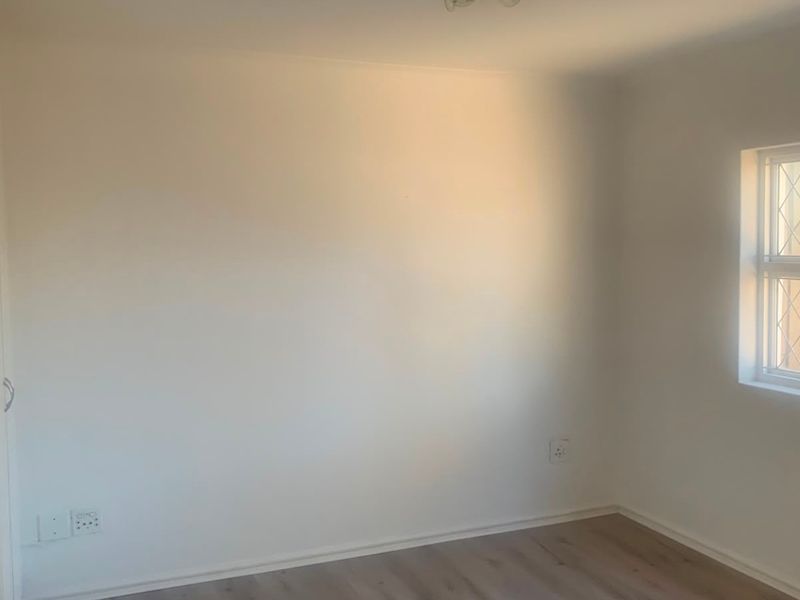 A clean, empty bedroom featuring neutral walls, laminate flooring, and a leaded glass window, providing a blank canvas for personalization.