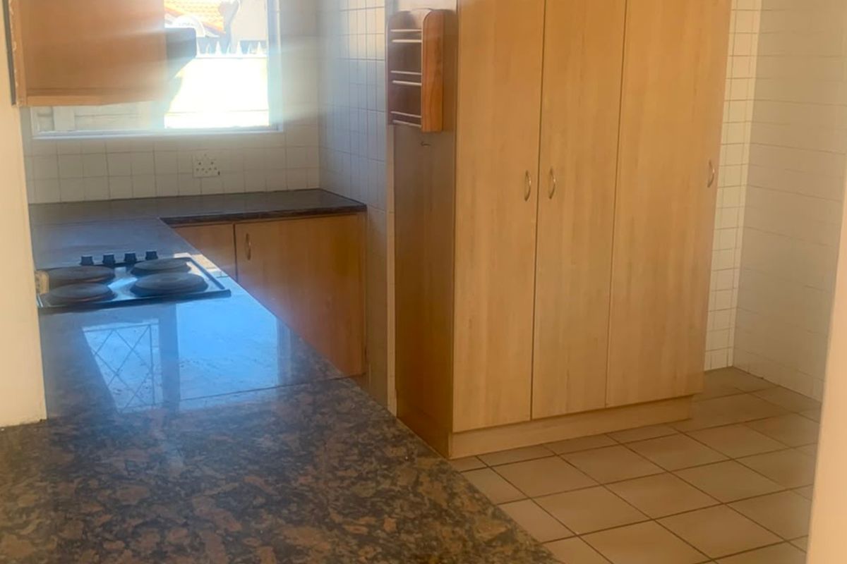 A functional kitchen featuring granite countertops, built-in wooden cabinetry, an electric hob, and tiled flooring, offering a blank canvas for potential updates.