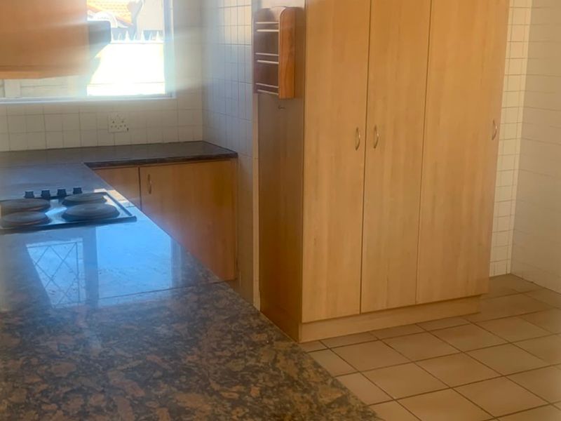 A functional kitchen featuring granite countertops, built-in wooden cabinetry, an electric hob, and tiled flooring, offering a blank canvas for potential updates.