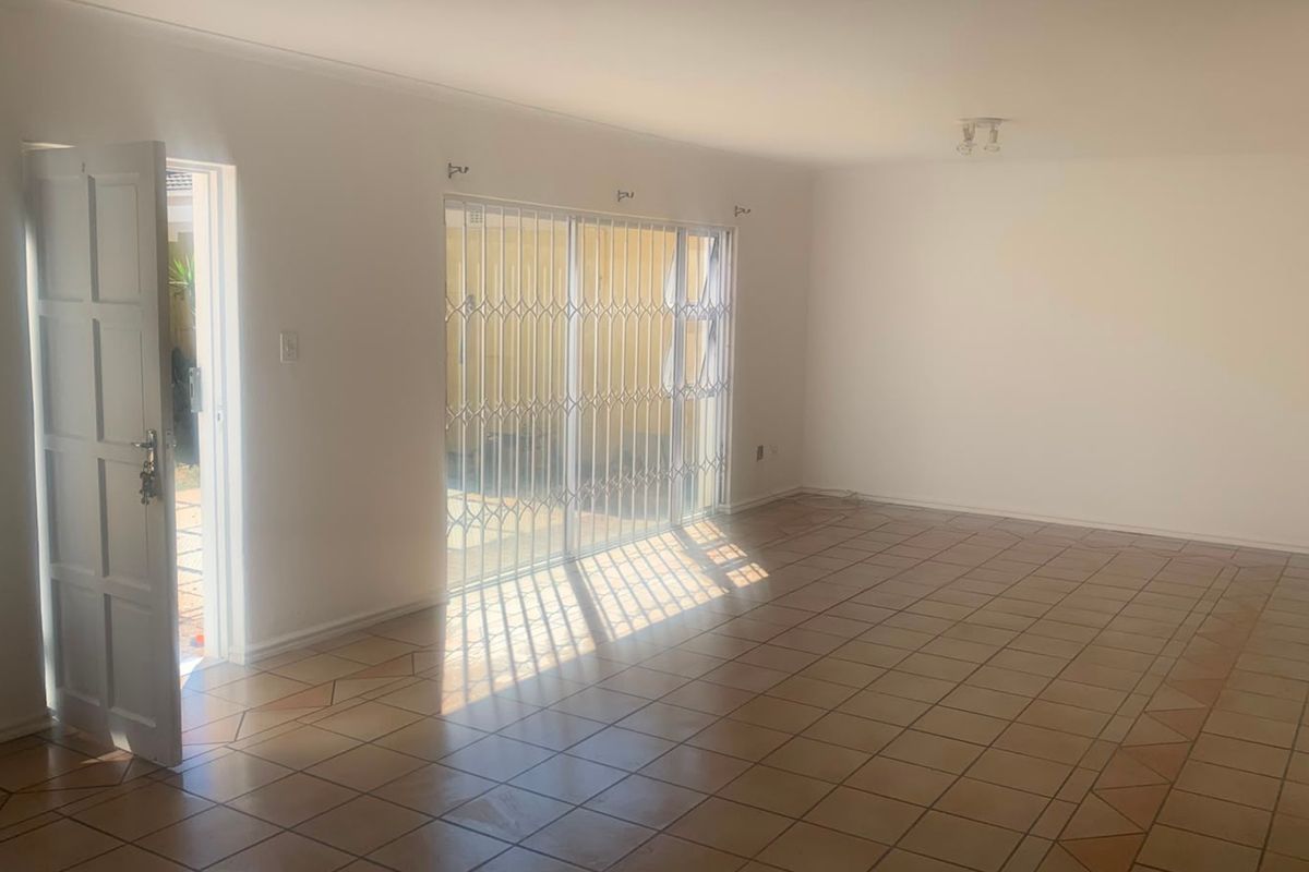 A spacious, empty living room featuring tiled flooring, a sliding glass door with security gate, and direct access to the exterior.