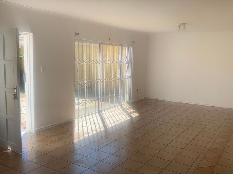 A spacious, empty living room featuring tiled flooring, a sliding glass door with security gate, and direct access to the exterior.