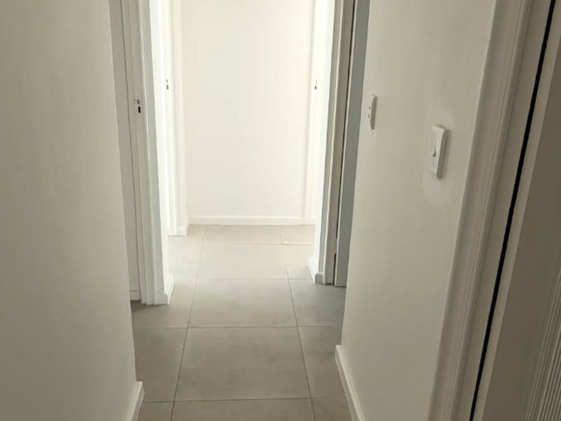 A clean, neutral hallway featuring light-toned floor tiles and white-painted walls, providing a bright and seamless transition between rooms.