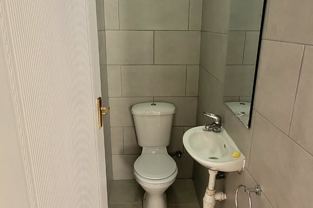 A compact guest bathroom featuring neutral wall tiles, a standard toilet, and a wall-mounted basin with a mirror.