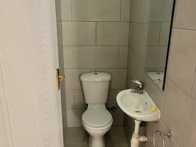 A compact guest bathroom featuring neutral wall tiles, a standard toilet, and a wall-mounted basin with a mirror.