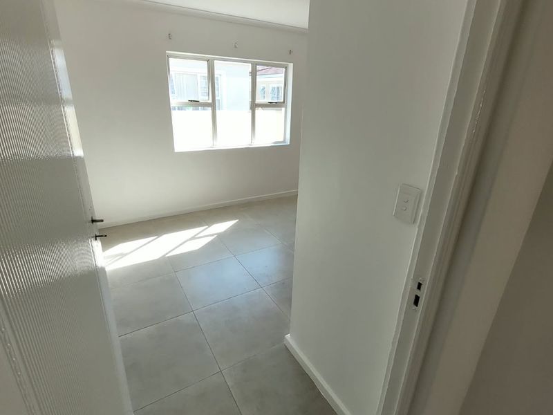 A bright, empty bedroom featuring neutral tiled flooring and aluminium window frames, offering a clean and versatile space ready for personalization.