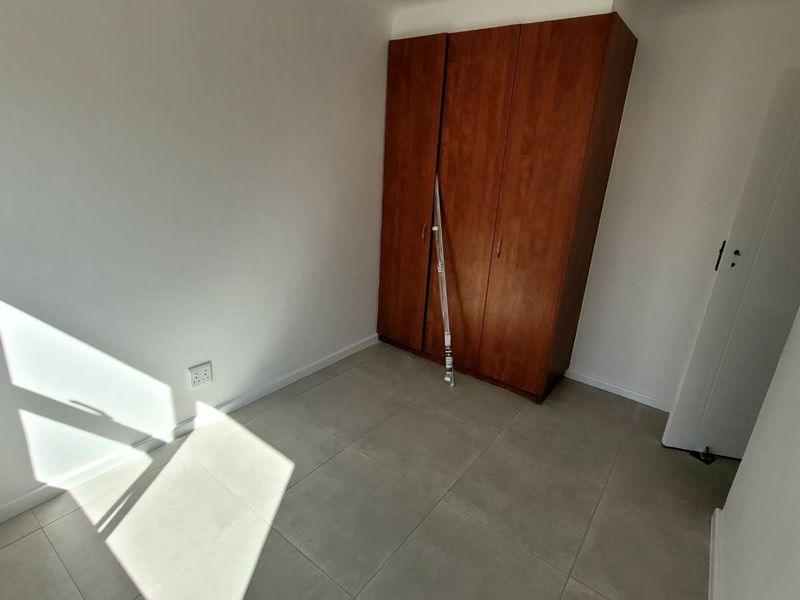 A bright, empty bedroom featuring neutral tiled flooring and a built-in wooden wardrobe.