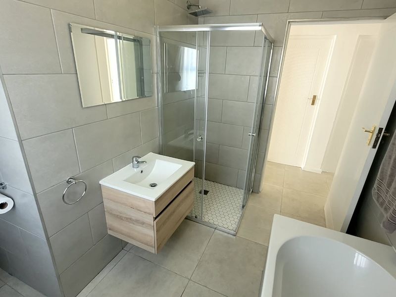 Modern bathroom featuring a wall-mounted vanity, glass shower enclosure with rain shower head, and a built-in bathtub with neutral grey tiling.