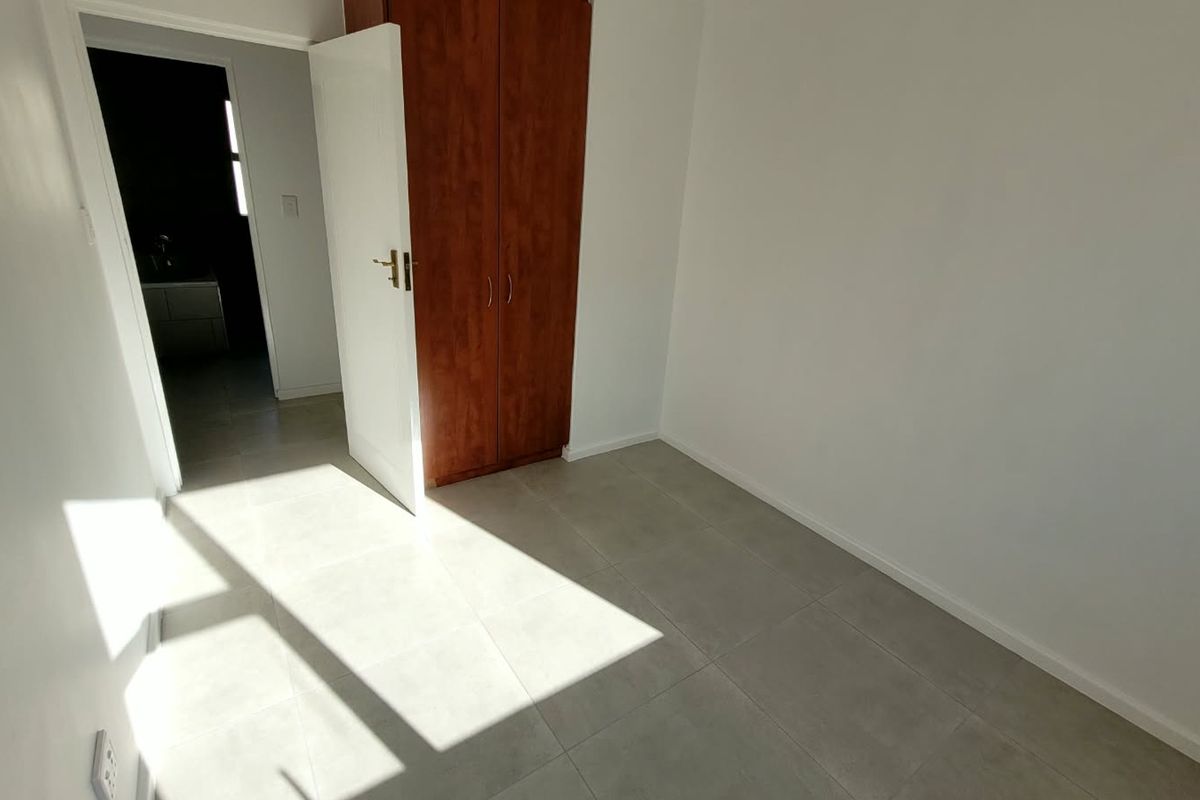 A bright, empty bedroom featuring neutral tiled flooring and a built-in wooden wardrobe, offering a clean and versatile space.