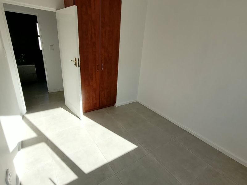 A bright, empty bedroom featuring neutral tiled flooring and a built-in wooden wardrobe, offering a clean and versatile space.