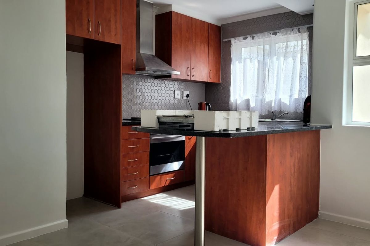 A functional kitchen featuring warm-toned wooden cabinetry, granite countertops, a breakfast bar, and a modern hexagonal tile backsplash with integrated stainless steel appliances.
