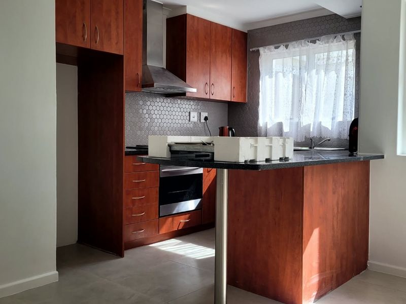 A functional kitchen featuring warm-toned wooden cabinetry, granite countertops, a breakfast bar, and a modern hexagonal tile backsplash with integrated stainless steel appliances.