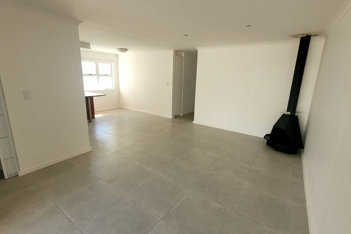 Spacious open-plan living area featuring neutral tiled flooring, a modern freestanding fireplace, and recessed lighting, offering a versatile blank canvas for interior design.