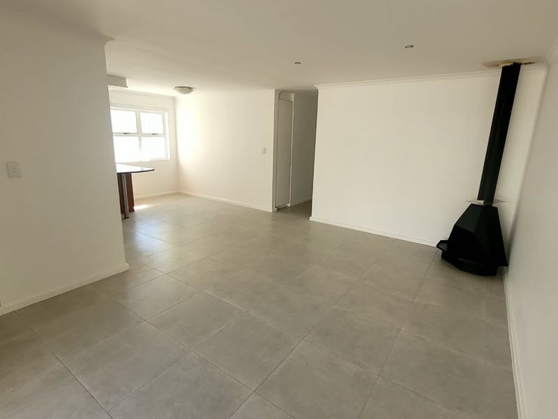 Spacious open-plan living area featuring neutral tiled flooring, a modern freestanding fireplace, and recessed lighting, offering a versatile blank canvas for interior design.