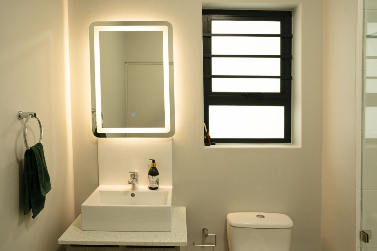 Modern bathroom featuring a vessel sink, stone-look vanity countertop, LED backlit mirror, toilet, and a glass-enclosed shower with contemporary finishes.