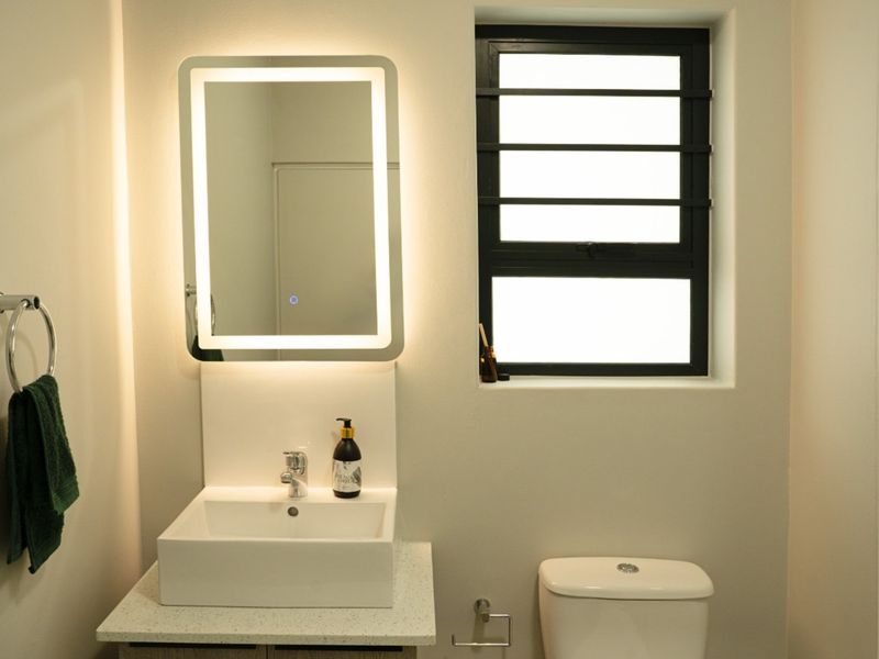 Modern bathroom featuring a vessel sink, stone-look vanity countertop, LED backlit mirror, toilet, and a glass-enclosed shower with contemporary finishes.