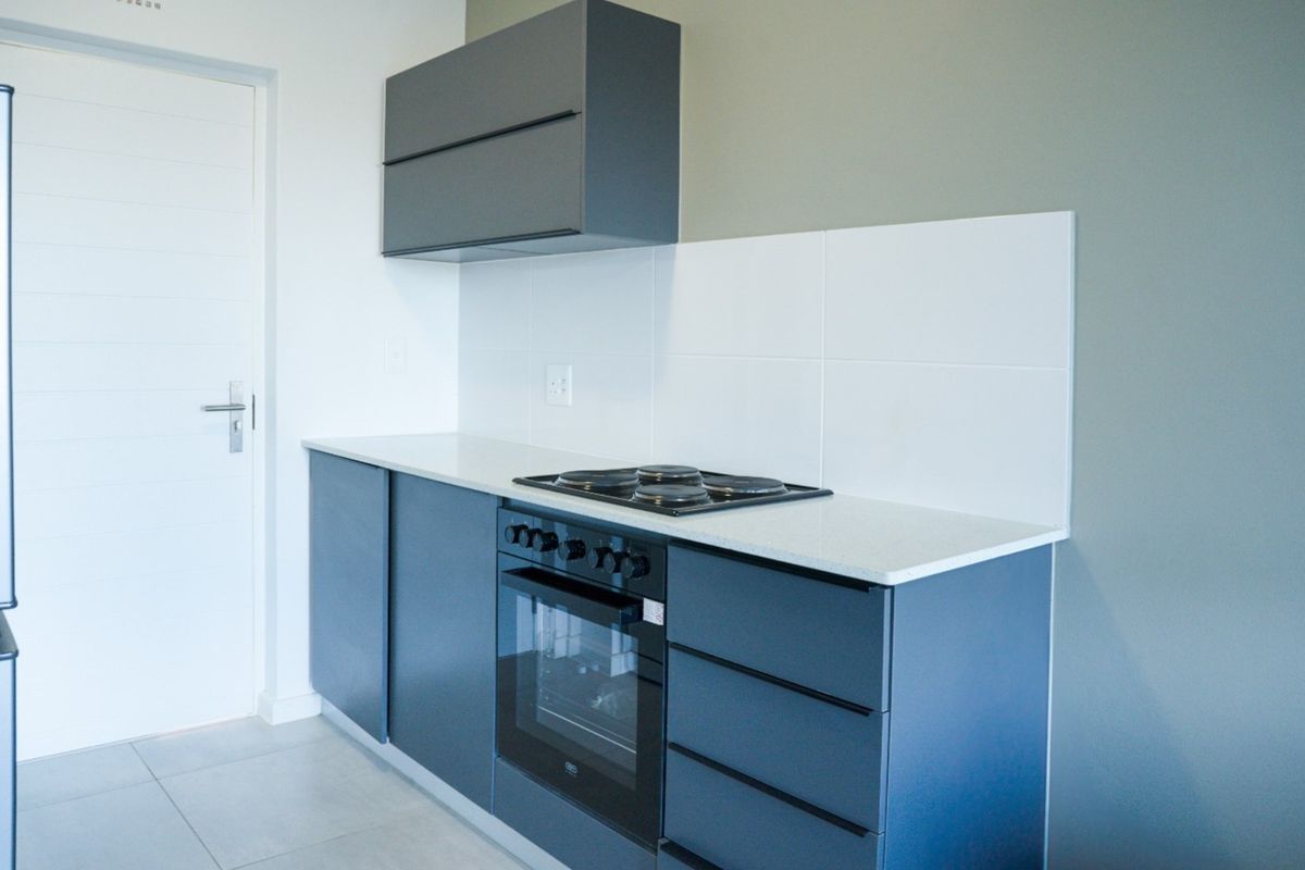 Modern kitchen featuring sleek grey cabinetry, stone countertops, a built-in oven, and an electric hob with a clean tiled splashback.
