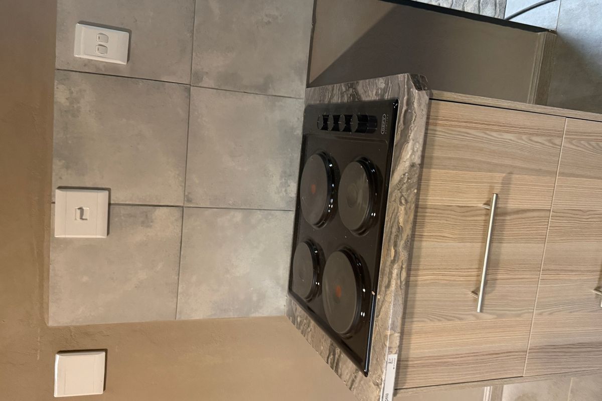 A modern kitchen section featuring a built-in electric hob, stone-look countertop, and light wood-grain cabinetry with a tiled splashback.