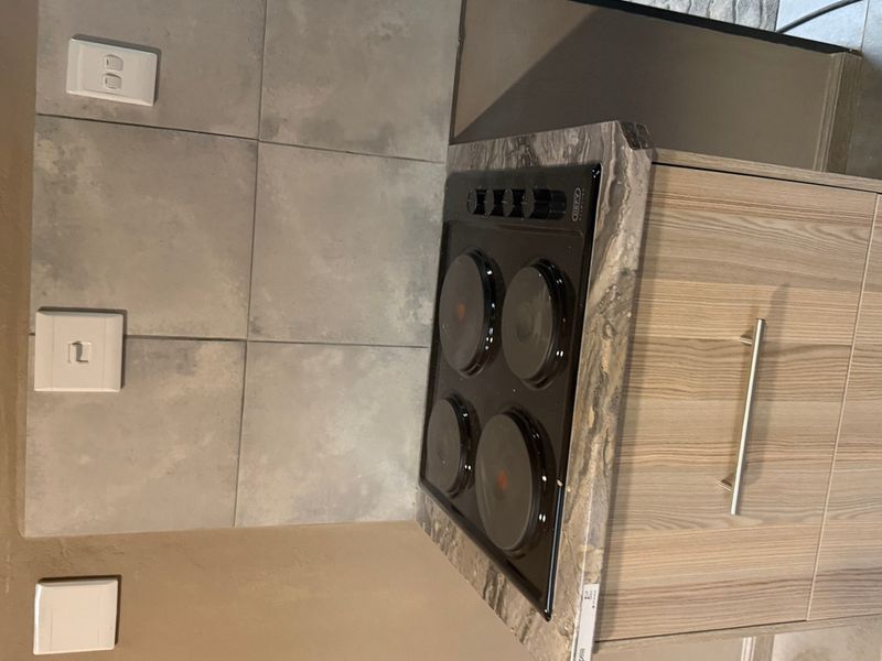 A modern kitchen section featuring a built-in electric hob, stone-look countertop, and light wood-grain cabinetry with a tiled splashback.