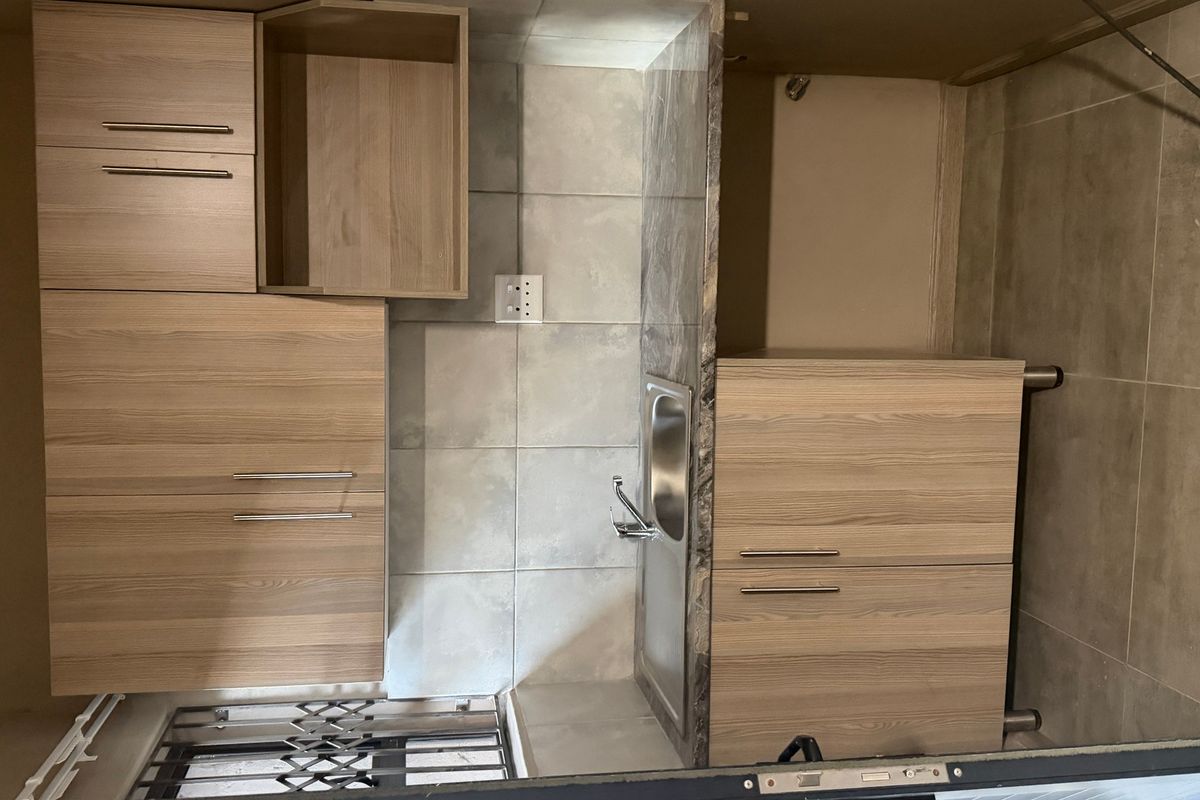 A compact kitchen area featuring modern wood-finish cabinetry, a stainless steel sink, and tiled splashbacks, providing a functional and clean workspace.