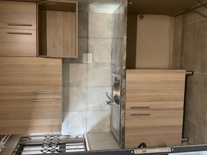 A compact kitchen area featuring modern wood-finish cabinetry, a stainless steel sink, and tiled splashbacks, providing a functional and clean workspace.