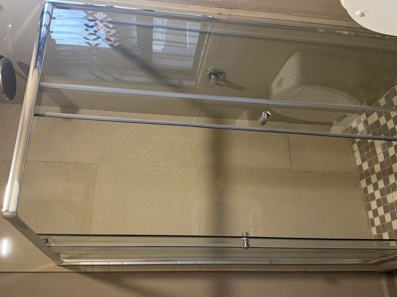 A bathroom featuring a glass shower enclosure, wall-mounted shower head, and a toilet with mosaic floor tiling.